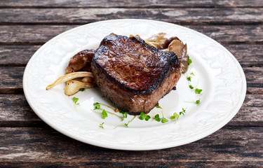 Tasty Beef Mignon steak with mushrooms and herbs on plate.