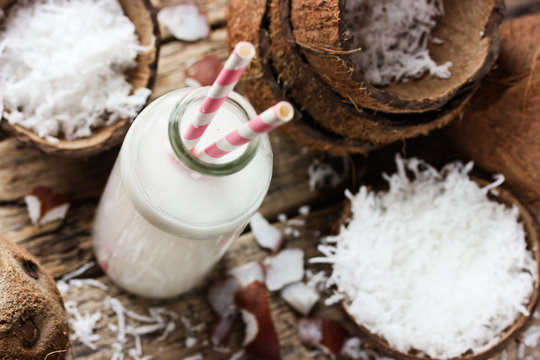 Coconut milk in bottle and fresh coconut chips on wooden table