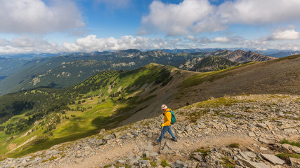 Hiker follows the trail towards Mount Rainier. Amazing view at the mountains which rose against the cloud sky.  MOUNT FREMONT LOOKOUT TRAIL, Sunrise Area, Mount Rainier