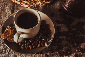 cup of coffee on textile with beans, dark candy sugar, pots, basket