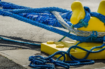Heavy blue ropes of an ocean-going passenger ship wrap around a yellow mooring bollard on a city pier in the harbor. - 111203630
