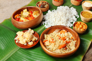 Boiled and fried rice with vegetables on banana leaf over wooden background