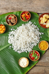 Boiled rice with vegetables and spices on banana leaf over wooden background
