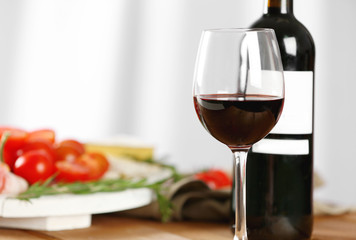 Glass and bottle of red wine with food on blurred background