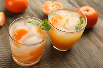 Two fresh delicious tangerine cocktails with ice, mint and mandarins on the wooden table, close up