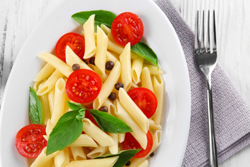 Plate of pasta with cherry tomatoes and basil leaves on table closeup