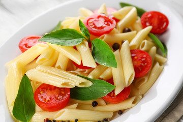 Plate of pasta with cherry tomatoes and basil leaves on table closeup
