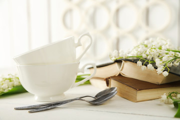 Porcelain cups with books and flowers on table
