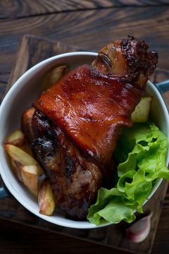 Above view of baked pork knuckle with potato wedges and salad