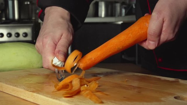 SLOW: A cook cleans a carrot on a cutting board in a restaurant kitchen