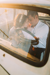 Portrait of young girl with floral headband and handsome man sitting in vintage car smiling...