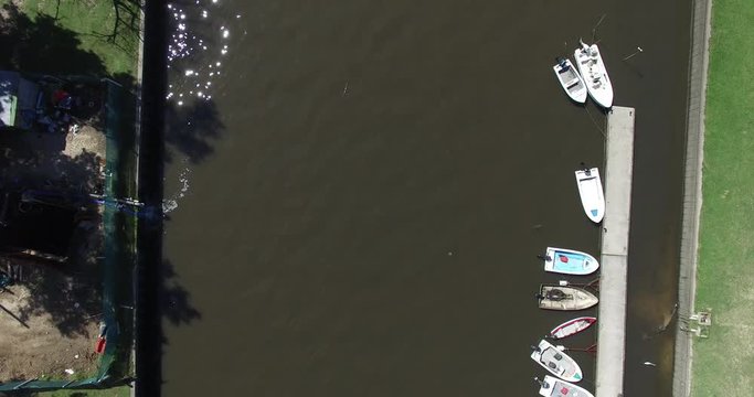 Aerial drone scene of little canal. Top view. Dock with boats, green shore and urban public space.