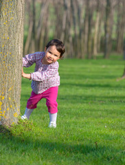 Little girl hiding behind a tree in a forest
