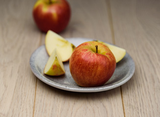 Fresh red Apple sliced on a plate spotted natural wooden background