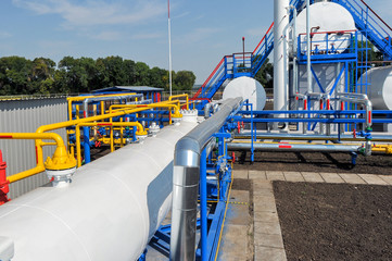 White fuel tanks and color gas pipes in natural gas treatment plant in bright sunny summer day
