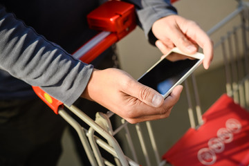 Closeup on person holding mobile phone in hand during shopping. Cart on background of store 