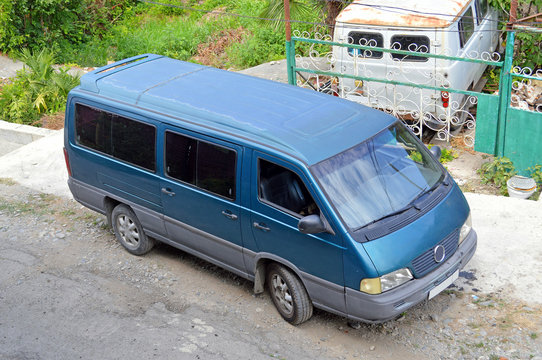 Микроавтобус стоит у ворот дачного участка в маленьком южном городке