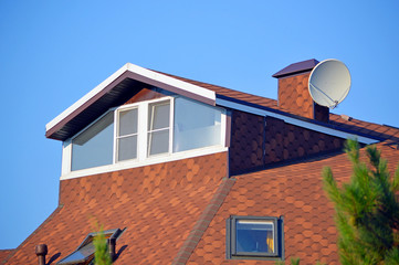 Окна мансардного этажа здания с коричневой крышей на фоне голубого неба