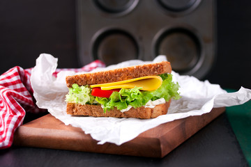 Toasted sandwich with salad leaves, tomatoes and cheese with fork on a cutting board on a dark background, closeup, horizontal