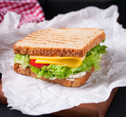 Toasted sandwich with salad leaves, tomatoes and cheese with fork on a cutting board on a dark background, closeup