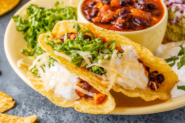 Tacos with chili con carne, salad, cheese and sour cream.