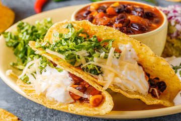 Tacos with chili con carne, salad, cheese and sour cream.