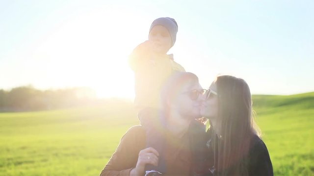 Happy joyful smiling young parents family father mother and little son on shoulders having fun outdoors in nature on green meadow grass background - slow motion 