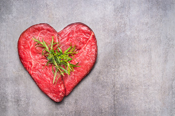 Obraz na płótnie Canvas Heart shape raw meat with herbs and text on gray concrete background , top view, horizontal