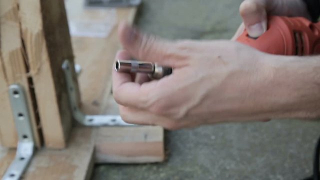 Man with Electric Drill is unscrewing the threaded screw from the wood.