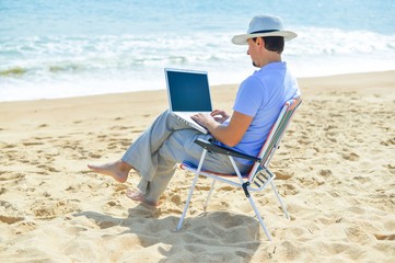 Back side view of relaxed man using laptop, beach background, outside summertime