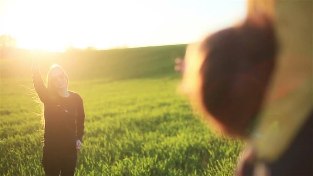 Happy mother waving hand goodbye or hallo to husband carrying son on shoulders - standing in green grass meadow background at sunset sun - distance divorce or reunion concept