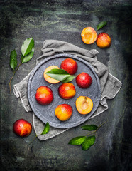 Halves of peaches or nectarines in gray stone plate with leaves, top view