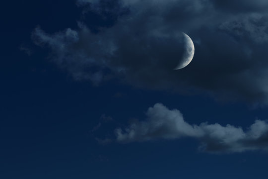 young growing moon in night sky with clouds, no stars