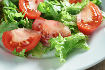 closeup photo of fresh summer salad with tomatoes, rucola and frillis leaves in plate on wood table, shallow focus