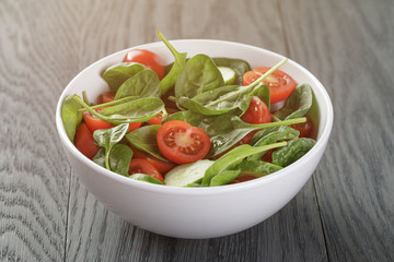 salad with tomato, spinach and cucumber in bowl on wood table, vintage toned photo
