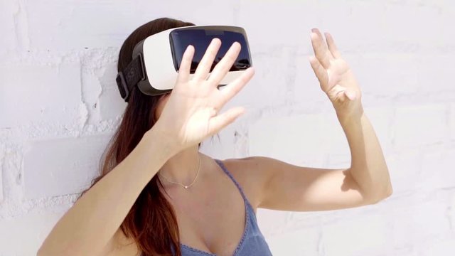 Young woman wearing virtual reality glasses walking along gesturing with her hands as she interacts with her virtual environment