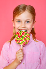 Funny little girl girl holding and eating colorful candy on pink background