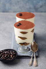 Tiramisu, traditional Italian dessert in glass on a grey stone background.