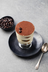 Tiramisu, traditional Italian dessert in glass on a grey stone background.