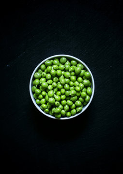 Fresh peeled green peas in white bowl on a black background, foo