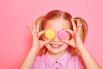 Girl with macaroons. Funny little girl holding colorful macaroons and closing her eyes on pink background.