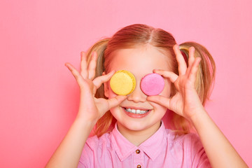 Girl with macaroons. Funny little girl holding colorful macaroons and closing her eyes on pink...