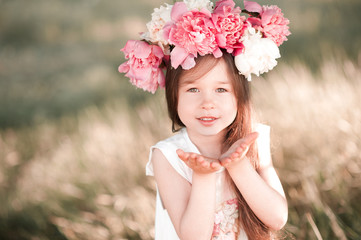 Naklejka premium Smiling baby girl 4-5 year old posing outdoors, wearing peony wreath. Looking at camera. Childhood. 