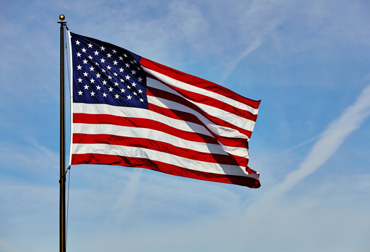 Flag USA in wind on flagpole with sky and clouds