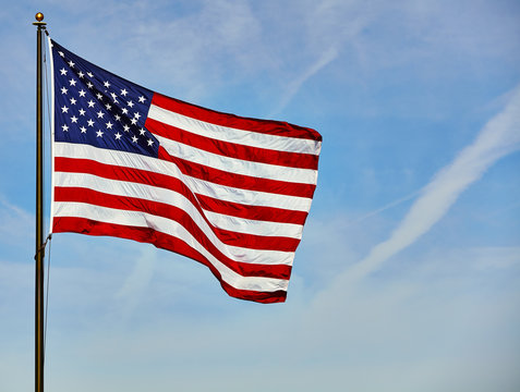 Flag USA waving in wind on pole with blue sky and clouds