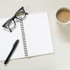 Blank notebook with eyeglasses,pen and cup of coffee on wooden table ( Space and composition for text )