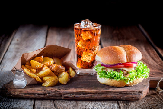 Burger with fries and cold drink on old wooden board