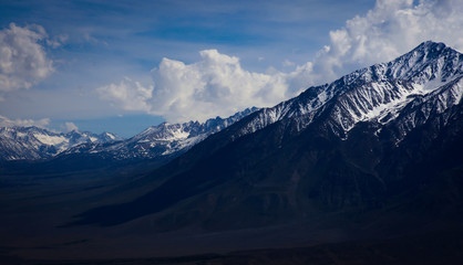 Snow covered mountain peaks overlooking a long deep valley with afternoon clouds building up