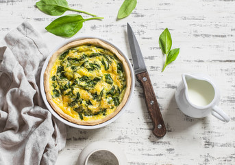 Pie with spinach, cheese and egg on a light wooden background