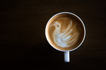 Cup of latte art coffee with froth shape bird and wooden backgro